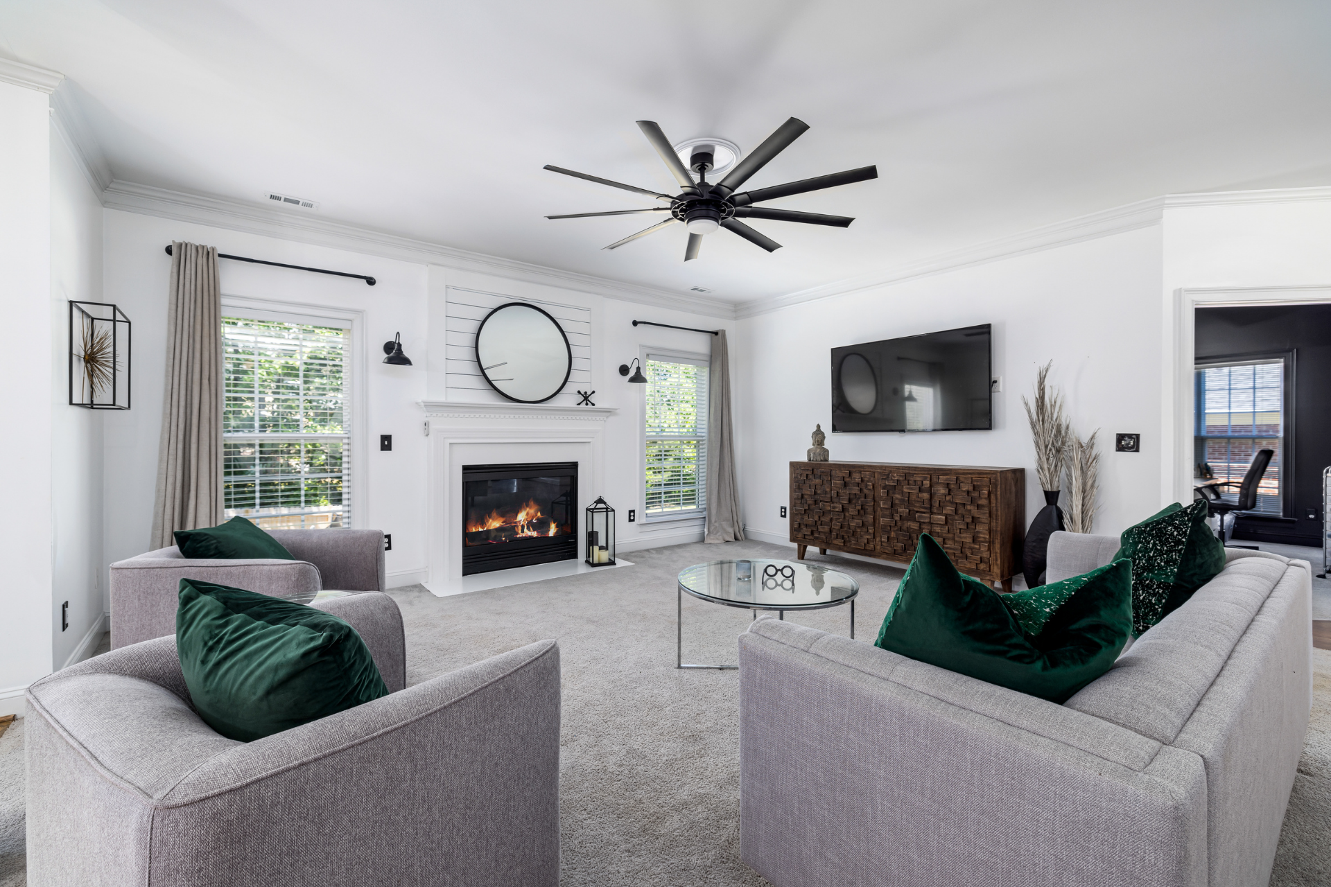 Bright living room with gray sofas, green pillows, fireplace, wall TV, and large clock on white walls