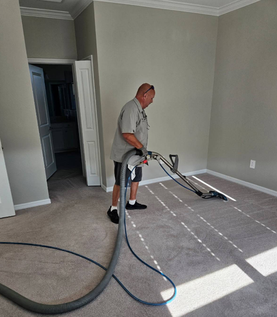 Worker cleaning carpet with a carpet extractor in a bright, empty room