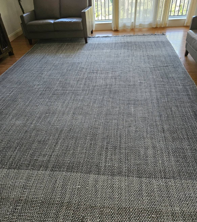 Gray textured area rug in a living room with sofas and sunlight from a glass door