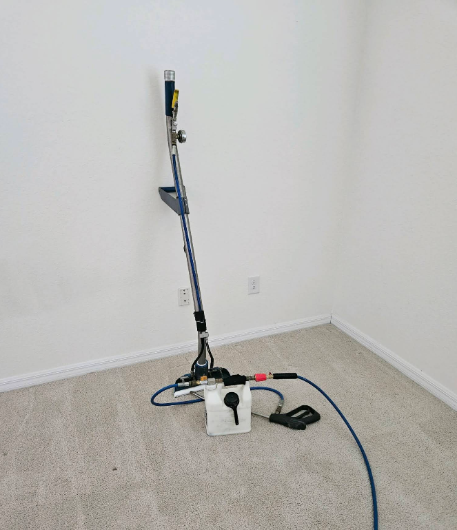 Vacuum cleaner, hose, and cleaning supplies in an empty corner room.