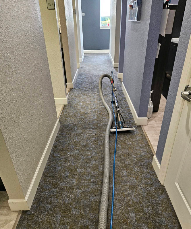 Vacuum cleaner on a carpeted hallway floor with a cord stretched along the corridor