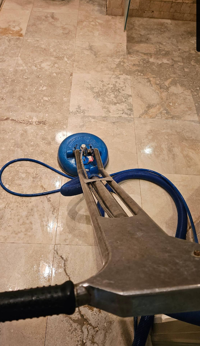 Blue floor-cleaning tool on beige tile floor with attached hose and metal handle