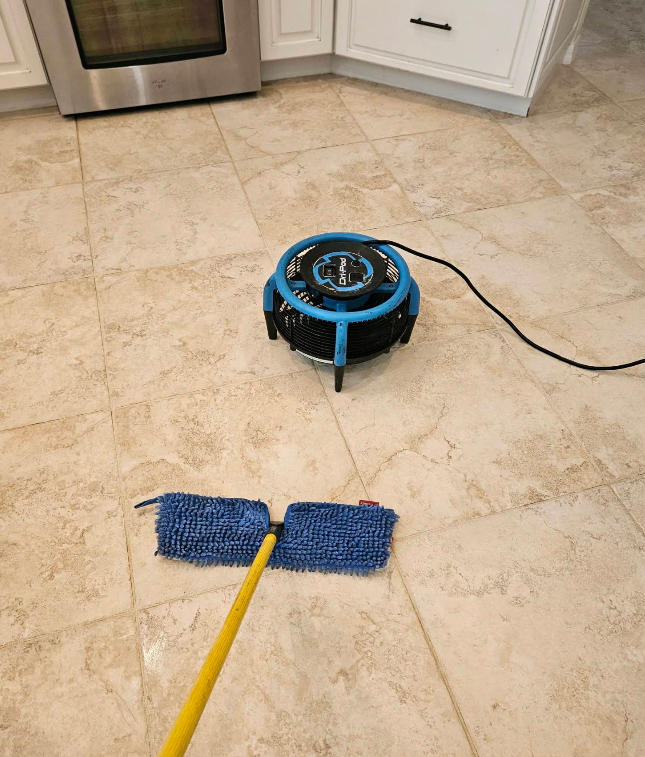 Blue floor-cleaning machine on a tiled kitchen floor next to a blue mop and yellow handle.
