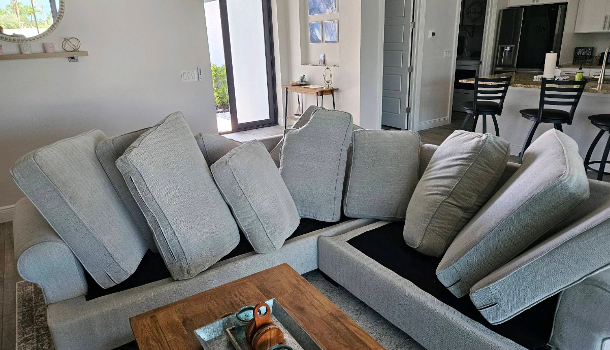 Gray sectional sofa with many throw pillows in a bright living room, with a wooden coffee table and open dining area.