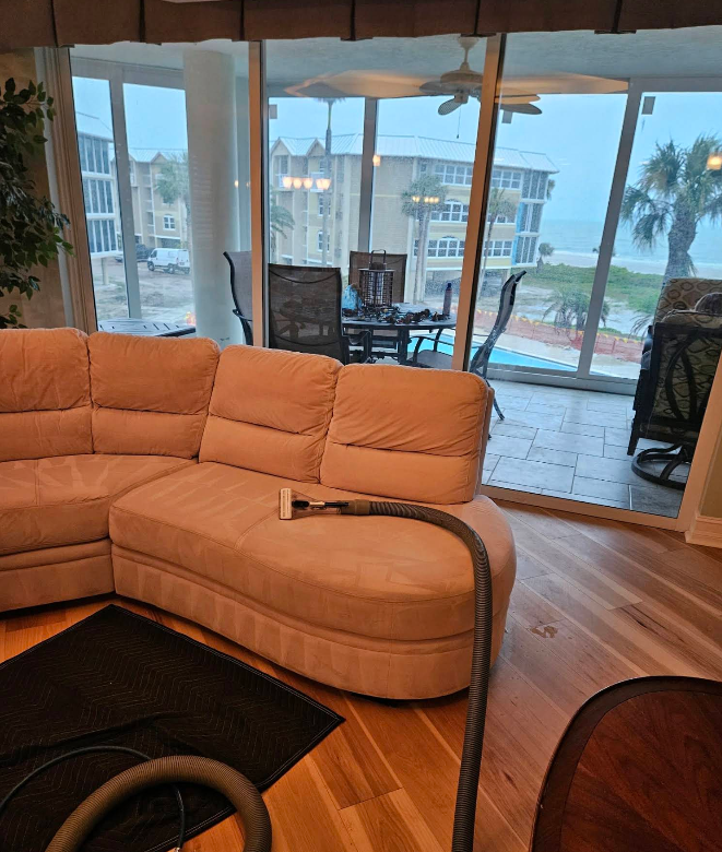Living room with a beige sectional sofa, wood floor, and large windows overlooking a pool and waterfront.