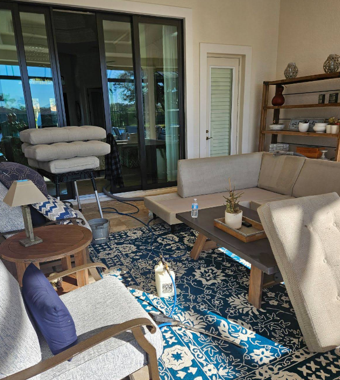 Bright patio living room with beige sofa, patterned blue rug, chairs, and glass doors to the outside