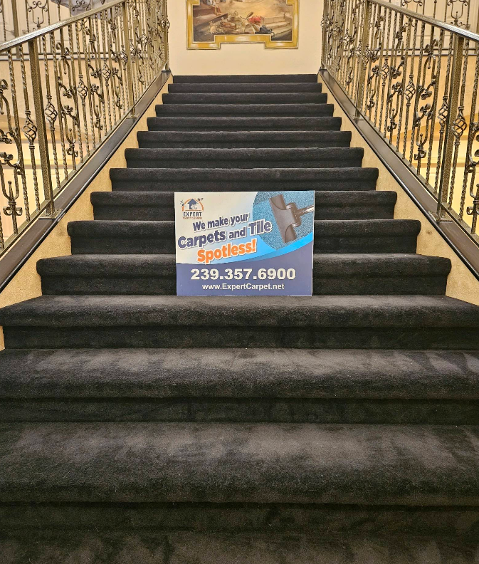 Carpeted staircase with ornate railings and a carpet cleaning sign displayed on the steps.