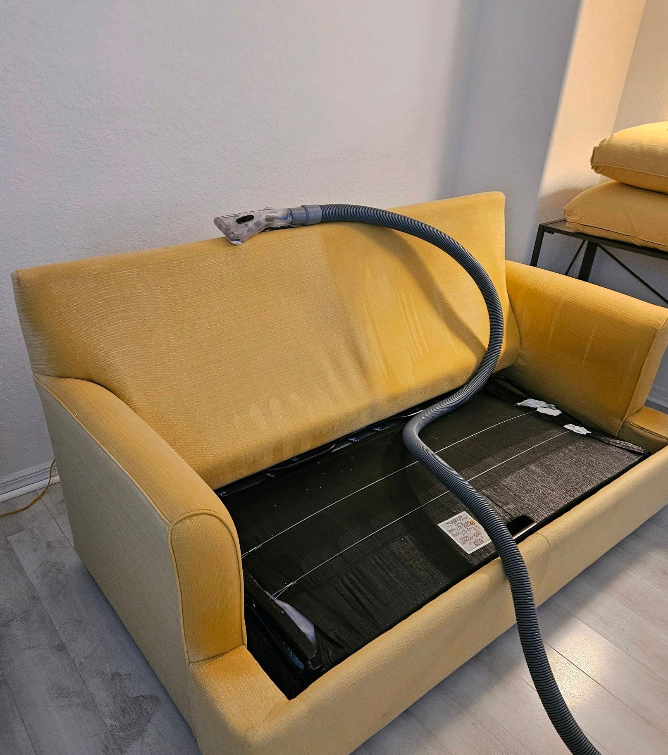 Yellow couch with cushions removed, exposing a black interior and a coiled hose on the backrest