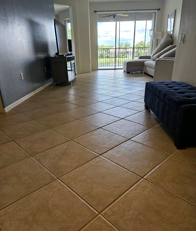 Empty tiled living room with a dark wall, gray sofa, and sliding glass doors opening to a balcony.