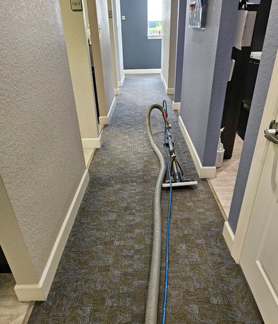 Carpeted hallway with a vacuum cleaner and blue hose stretched along the floor.