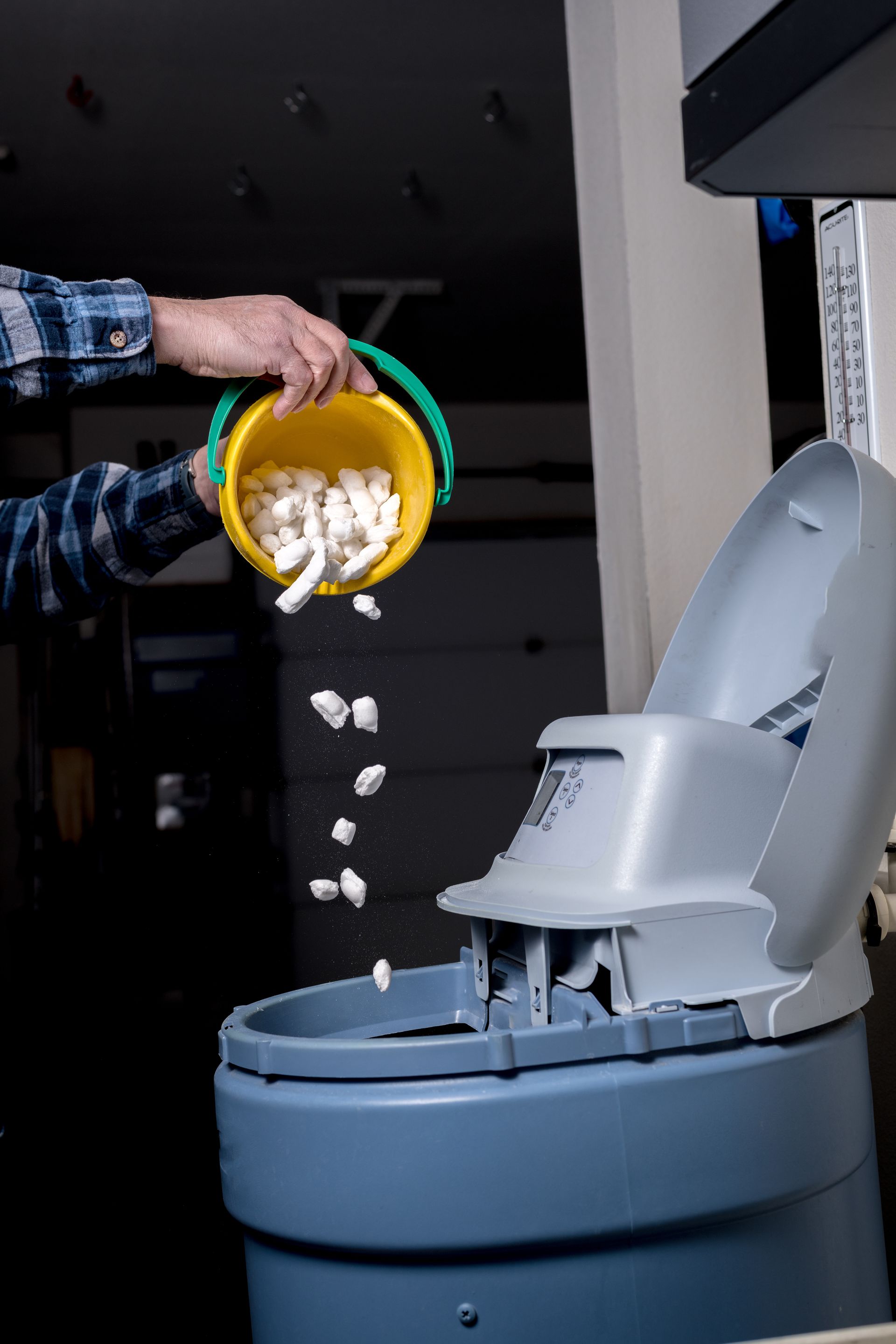 Hand dropping white granules into an open gray litter box with a raised lid