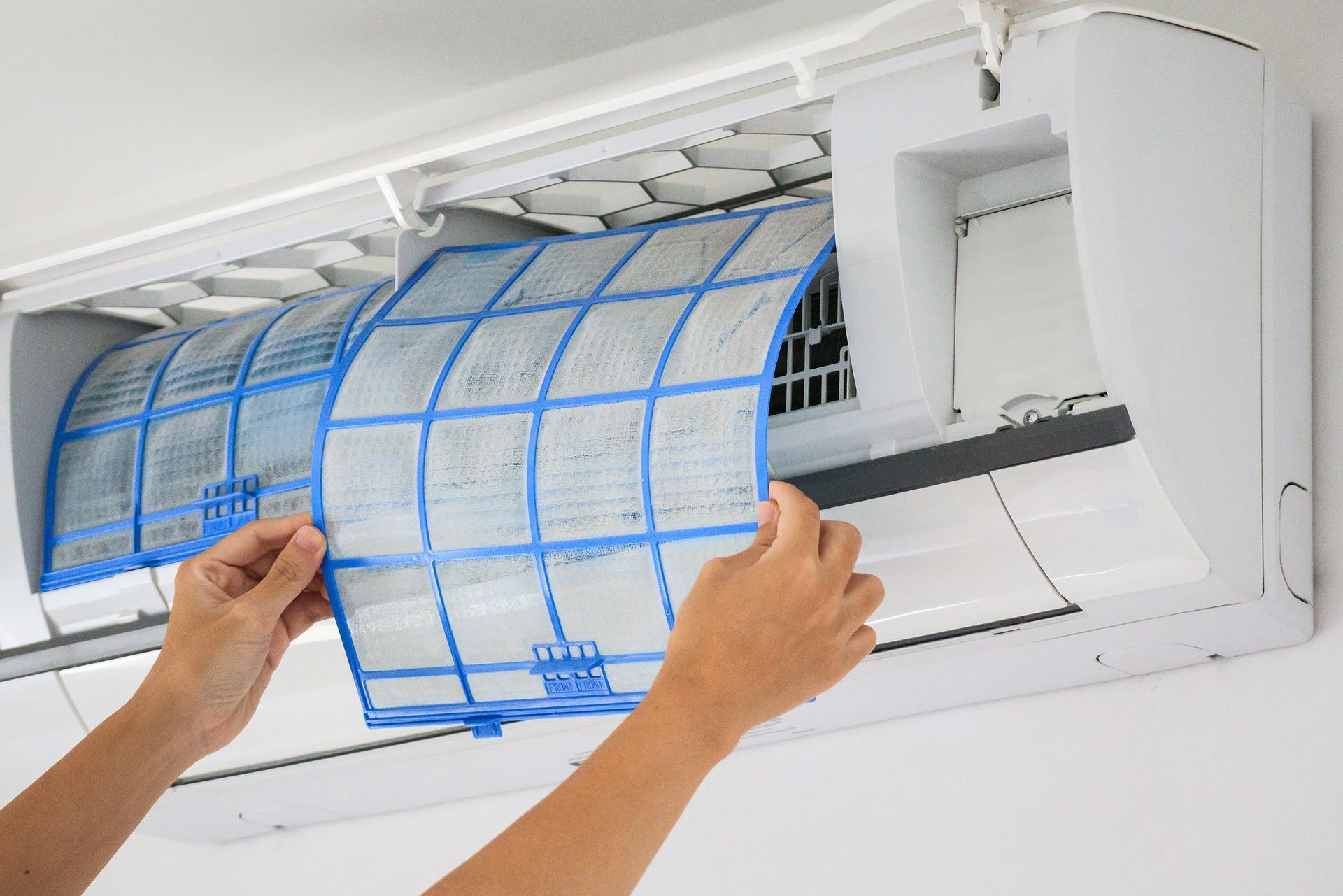 Hands removing a blue mesh air conditioner filter from a wall unit