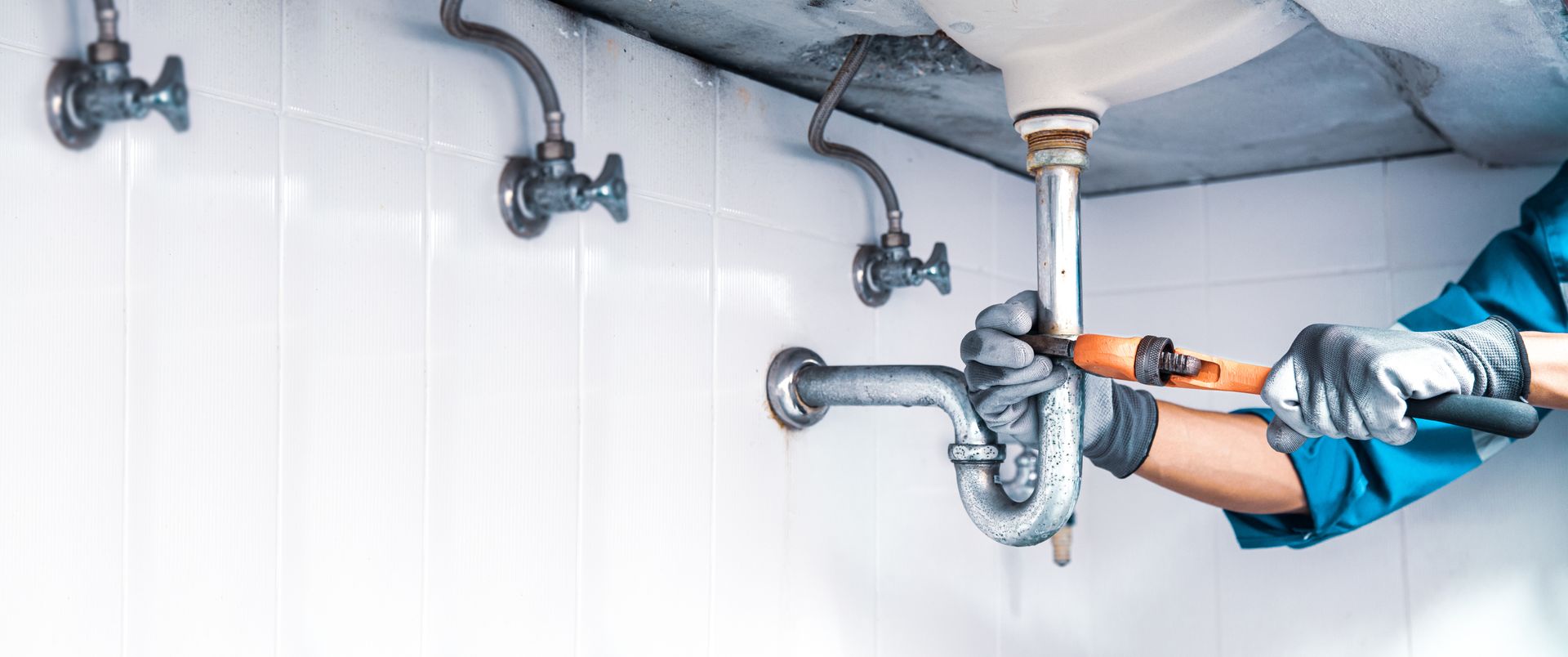 Experienced plumber fixing under-sink drainage system with a wrench during residential service.