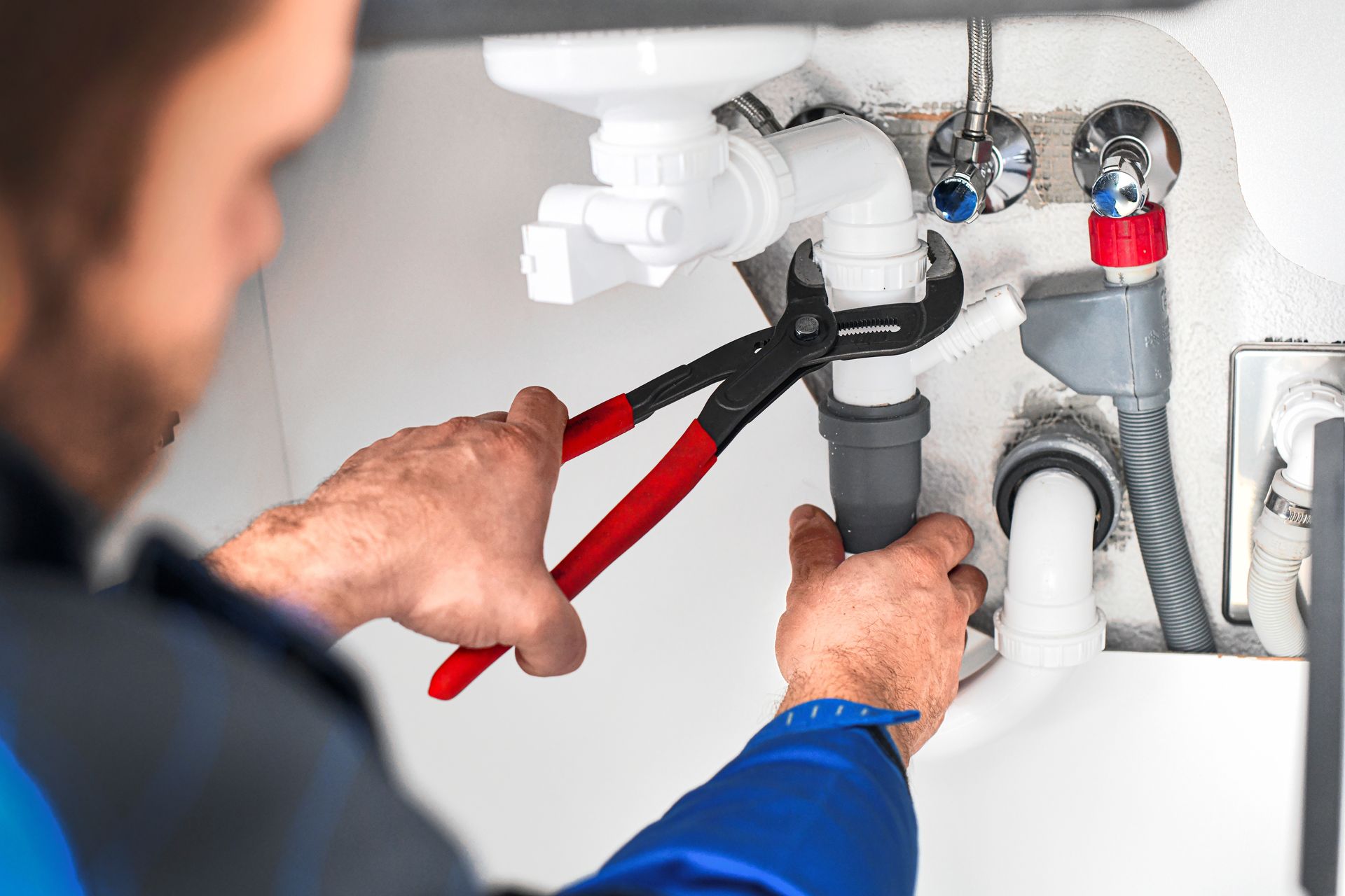Professional commercial plumber using a wrench to repair complex under-sink pipe infrastructure.