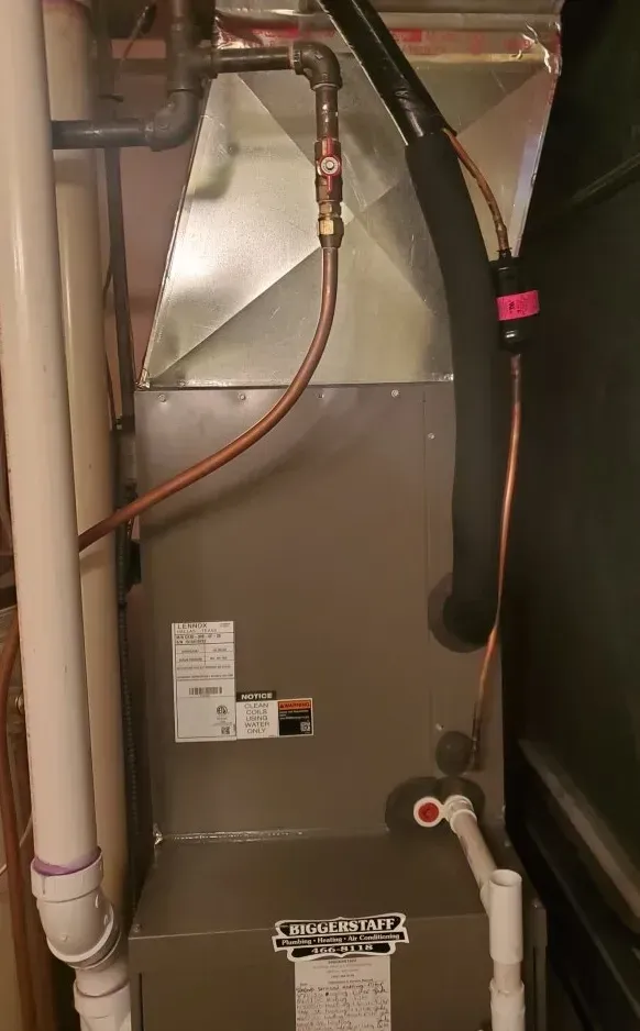 Utility closet with a gray HVAC unit, copper pipes, and white drain lines in a tight indoor space