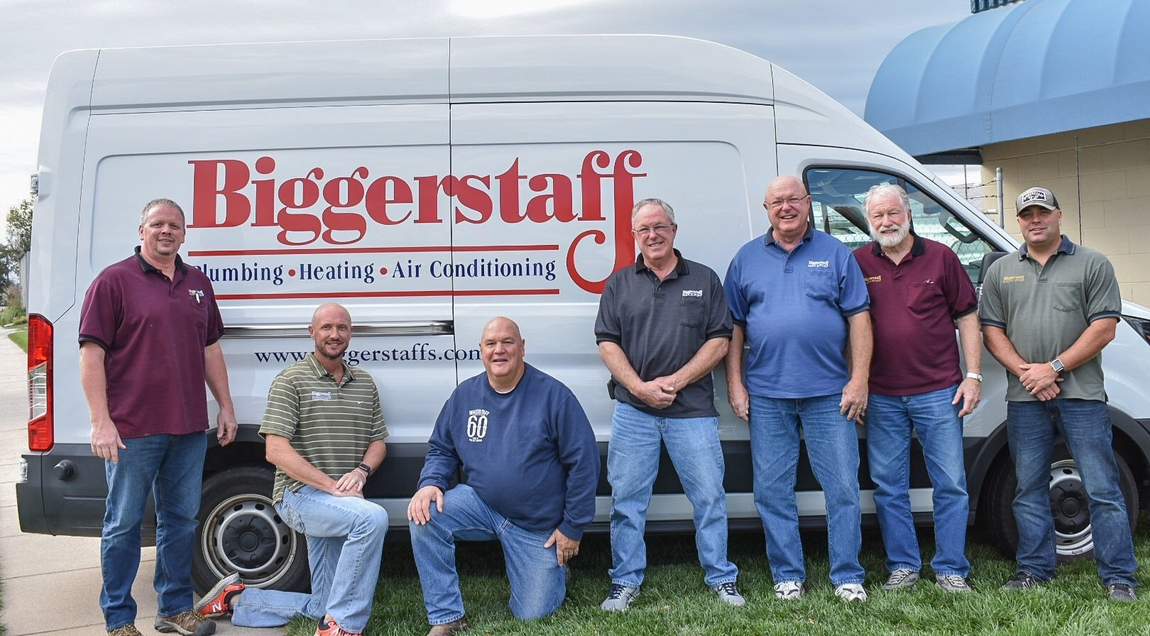 Seven workers pose in front of a Biggerstaff service van, standing and crouching outdoors.