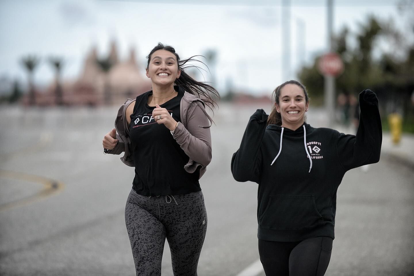 Two women are running down a street together and smiling.