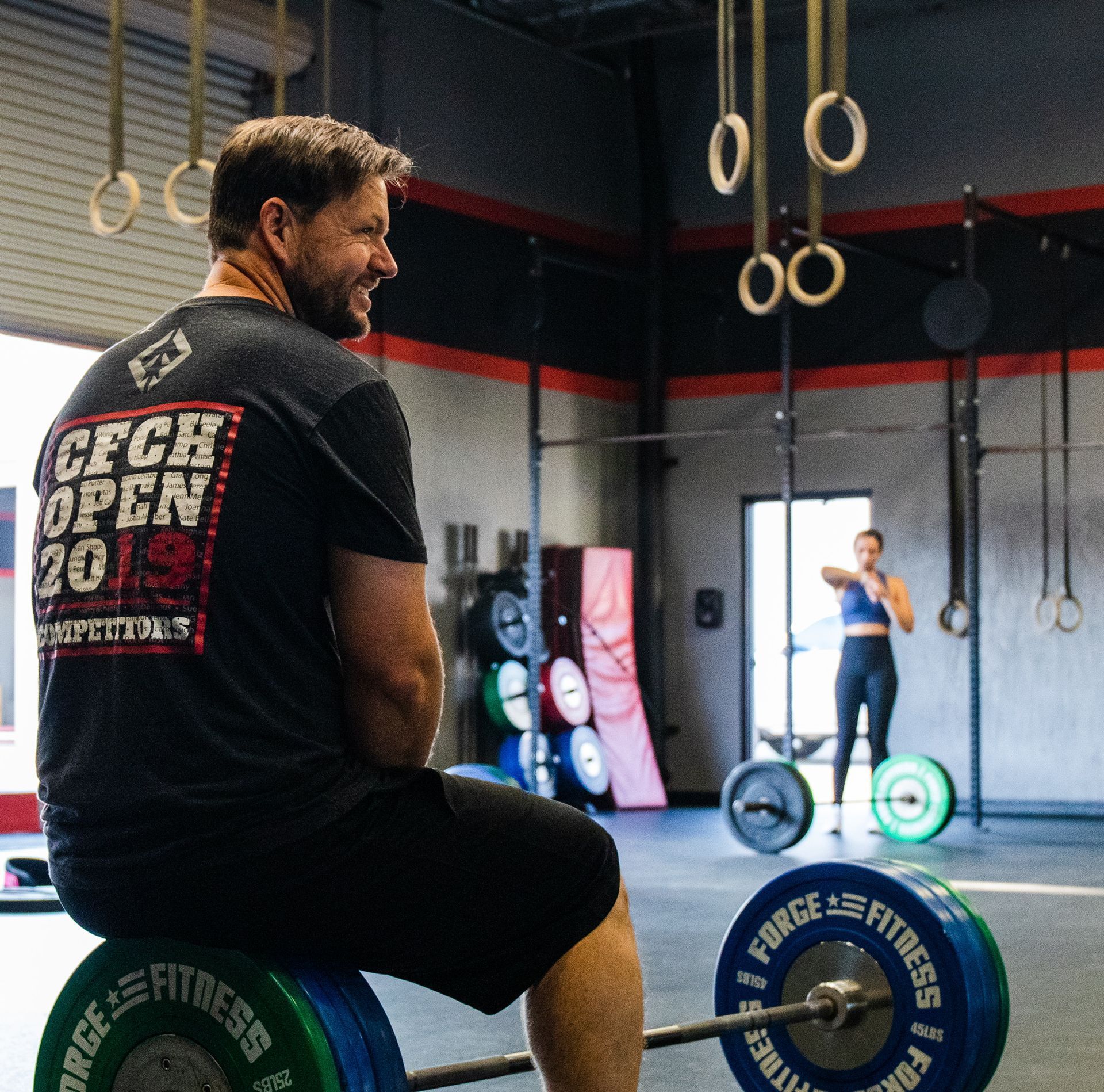 A man wearing a cfch open shirt sits on a barbell