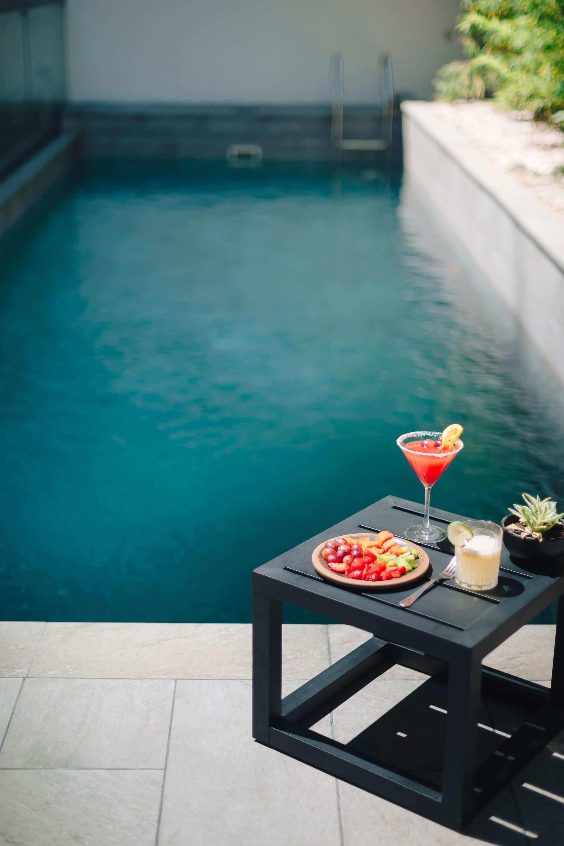 Una mujer con un traje de baño rosa y sombrero está sentada en un sillón junto a una piscina.