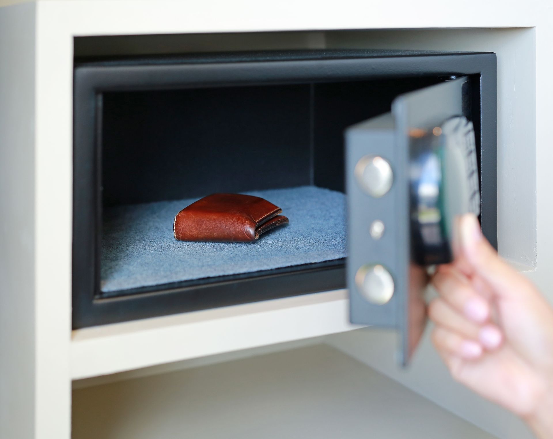 A secure brown wallet safely stored inside a half-closed safe, with a person grasping the handle of the safe box. A secure brown wallet safely stored inside a half-closed safe, with a person grasping the handle of the safe box.