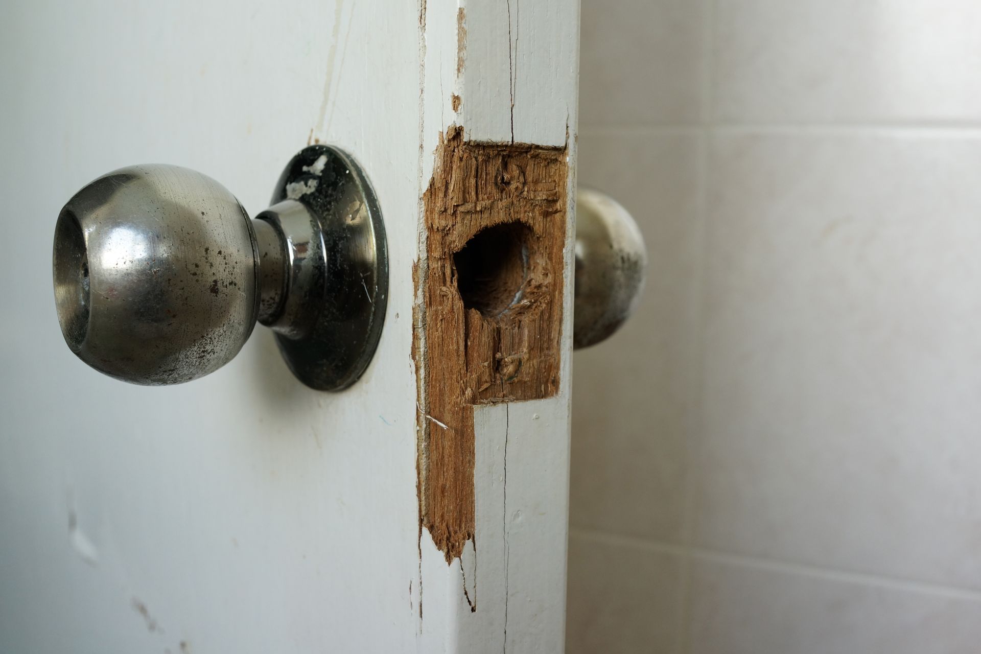 A damaged door with missing pieces of a doorknob, including the crucial latch mechanism that prevents the door from opening, requiring locksmith repair.
