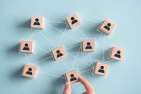 Hand arranging wooden blocks with person icons connected by lines on a blue background.