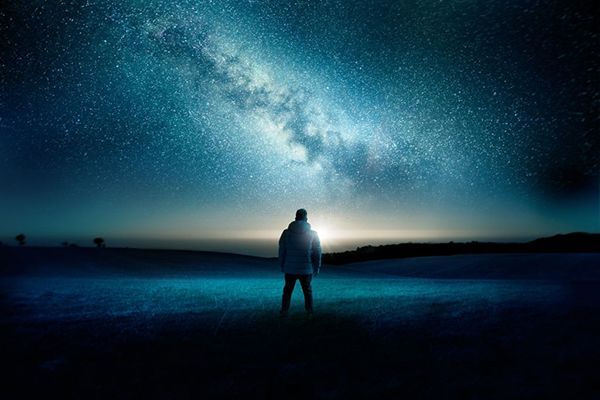 Person standing outdoors, gazing at the Milky Way galaxy in a starry night sky.