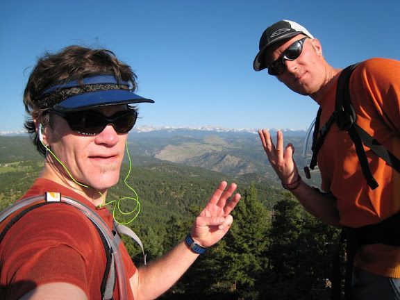 Two hikers in sunglasses posing on a mountain trail with valley and peaks in the background