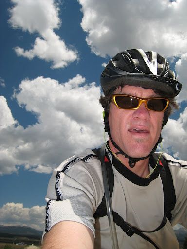Cyclist wearing helmet and sunglasses against a cloudy blue sky