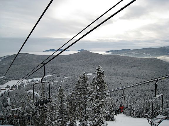 Ski lift over snowy mountain landscape with snow-covered trees and distant hills