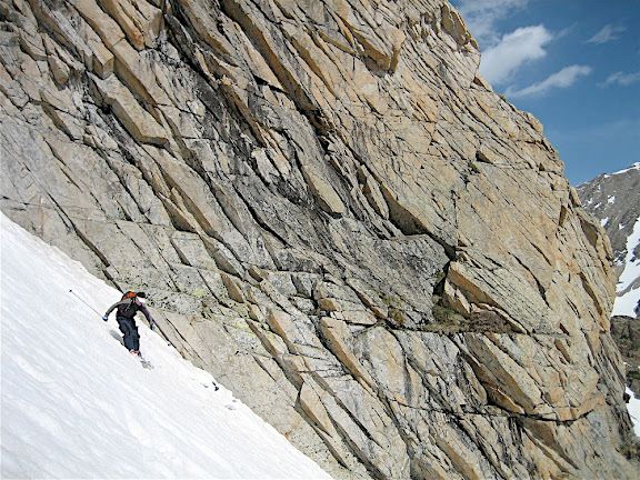 Climber traversing a steep snowy slope beside a rocky cliff