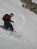 Skier in black and red gear descending a snowy slope with poles.