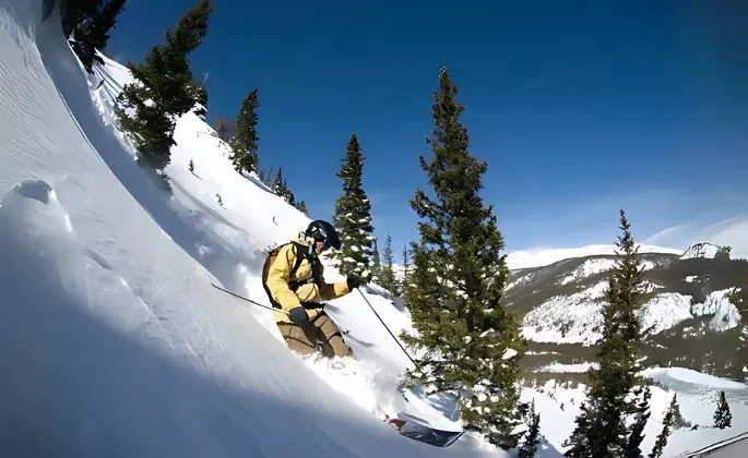 Skier carves down a steep, snow-covered mountain slope on a sunny day.