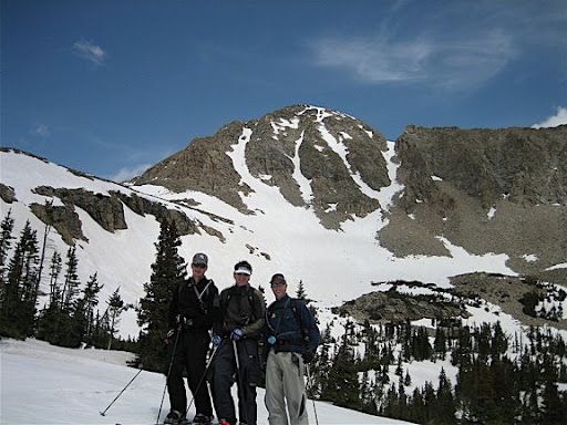 Three skiers standing on snowy mountain slope under a blue sky