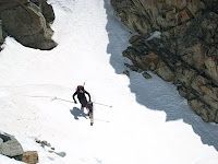 Skier traversing a snowy mountain slope beside rocky cliffs