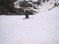 Skier descending a snowy mountain slope with rocky cliffs in the background