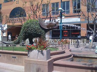 Urban plaza with a fountain, abstract sculpture, and brick buildings in the background