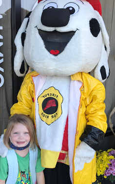 A little girl is posing for a picture with a fireman mascot