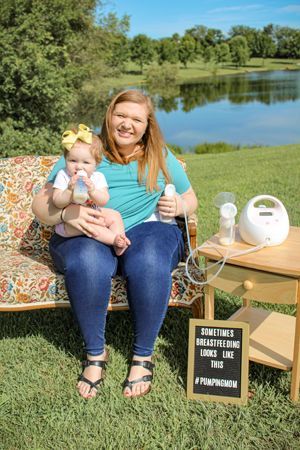 A woman is sitting on a couch holding a baby and a breast pump.