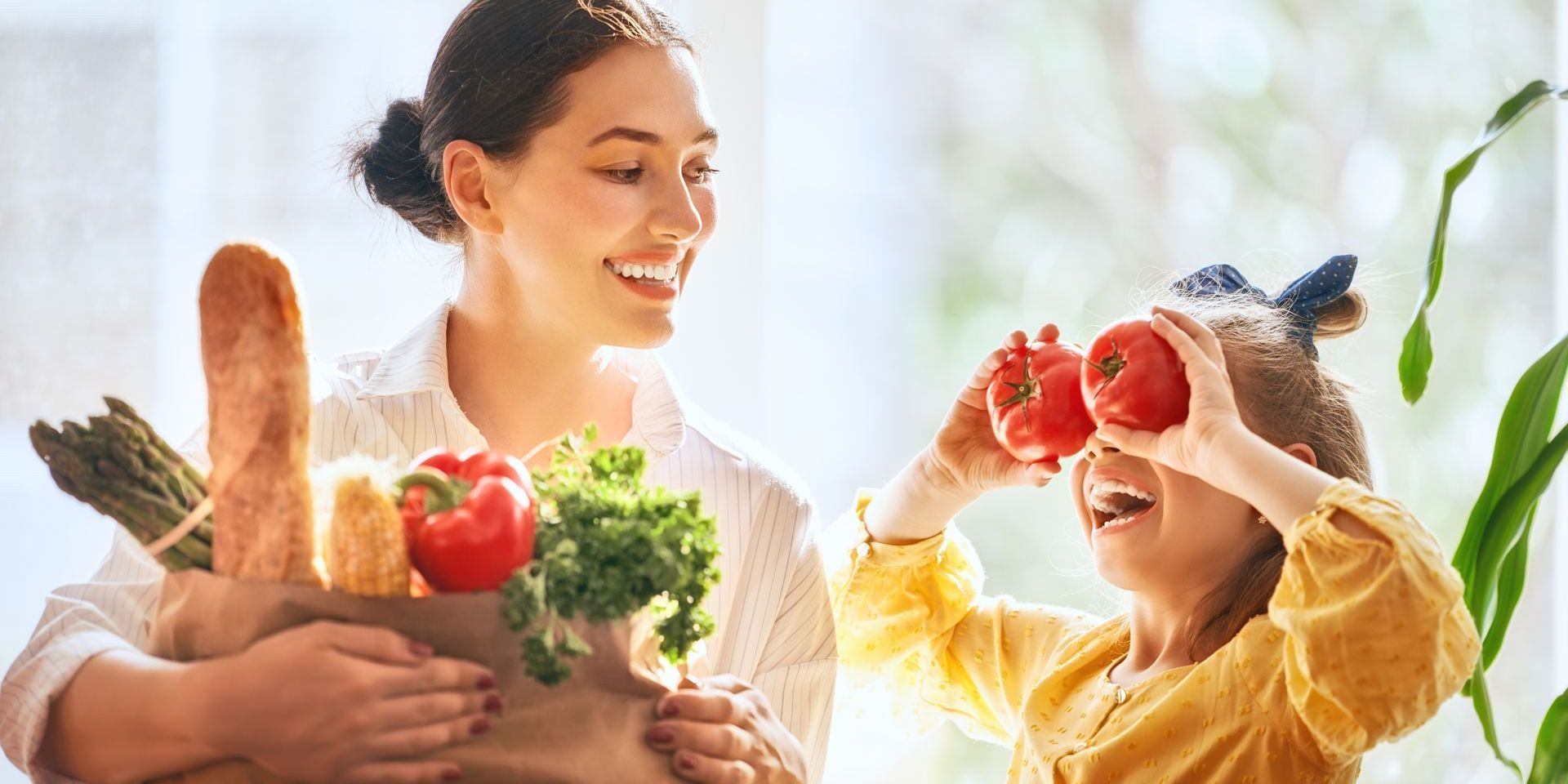A woman and a little girl are holding a bag of groceries.