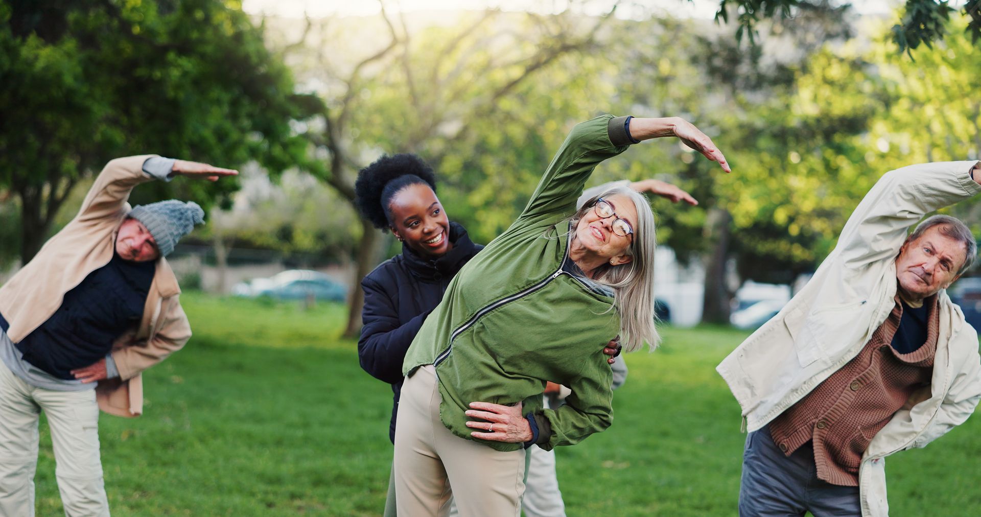 A group of people are doing stretching exercises in a park.