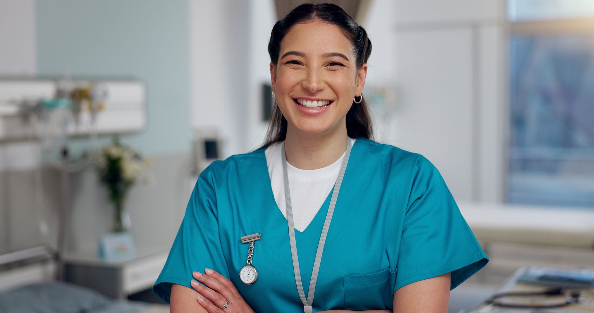 A nurse is smiling with her arms crossed in a hospital room.