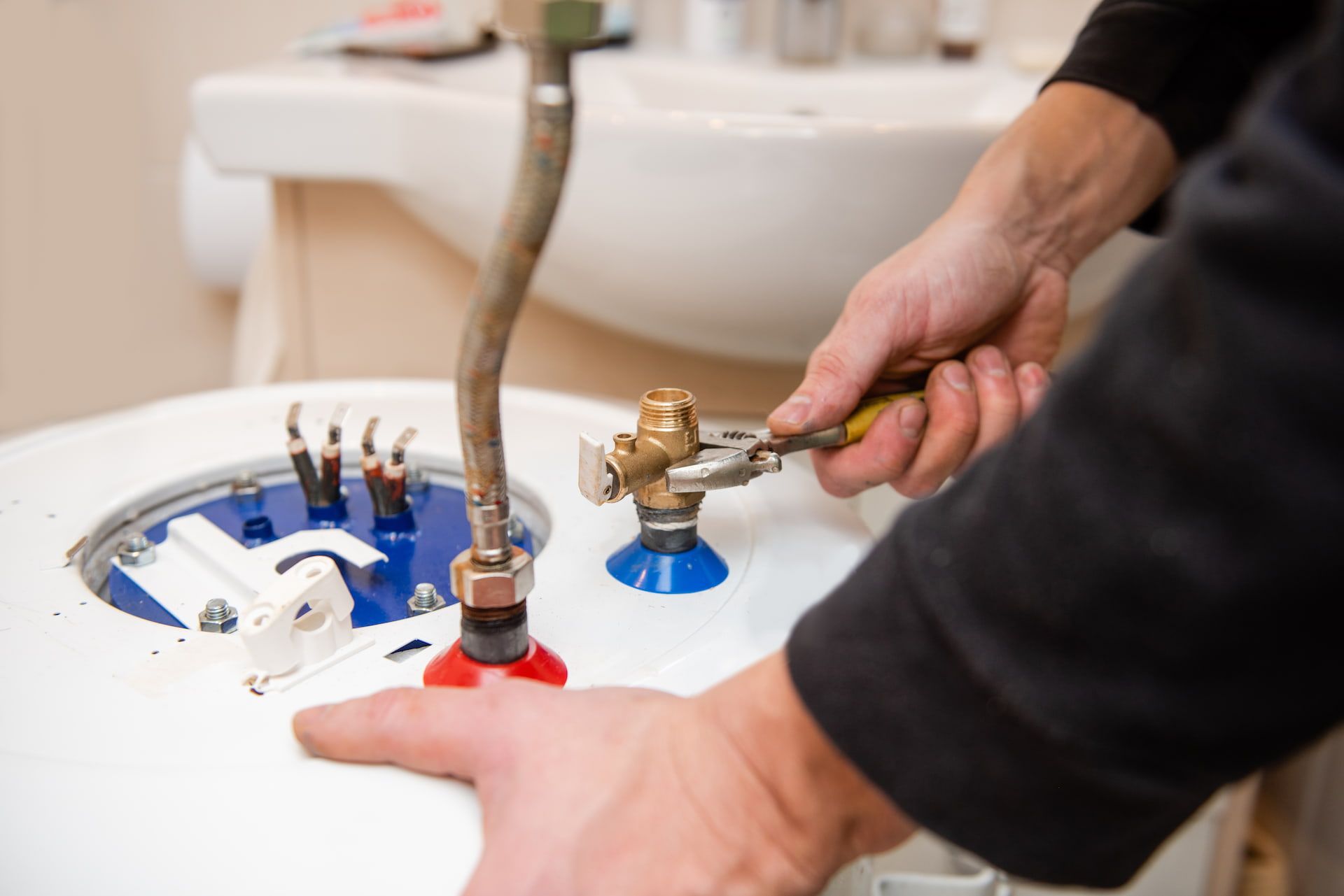 Plumber working on a hot water heater, using a wrench.