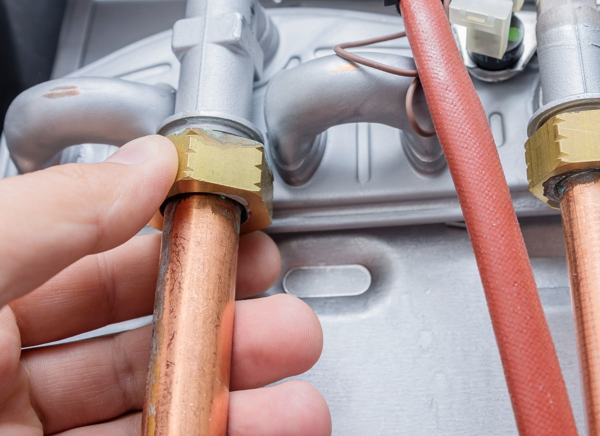 Hand tightening a brass nut on a copper pipe connected to a boiler.