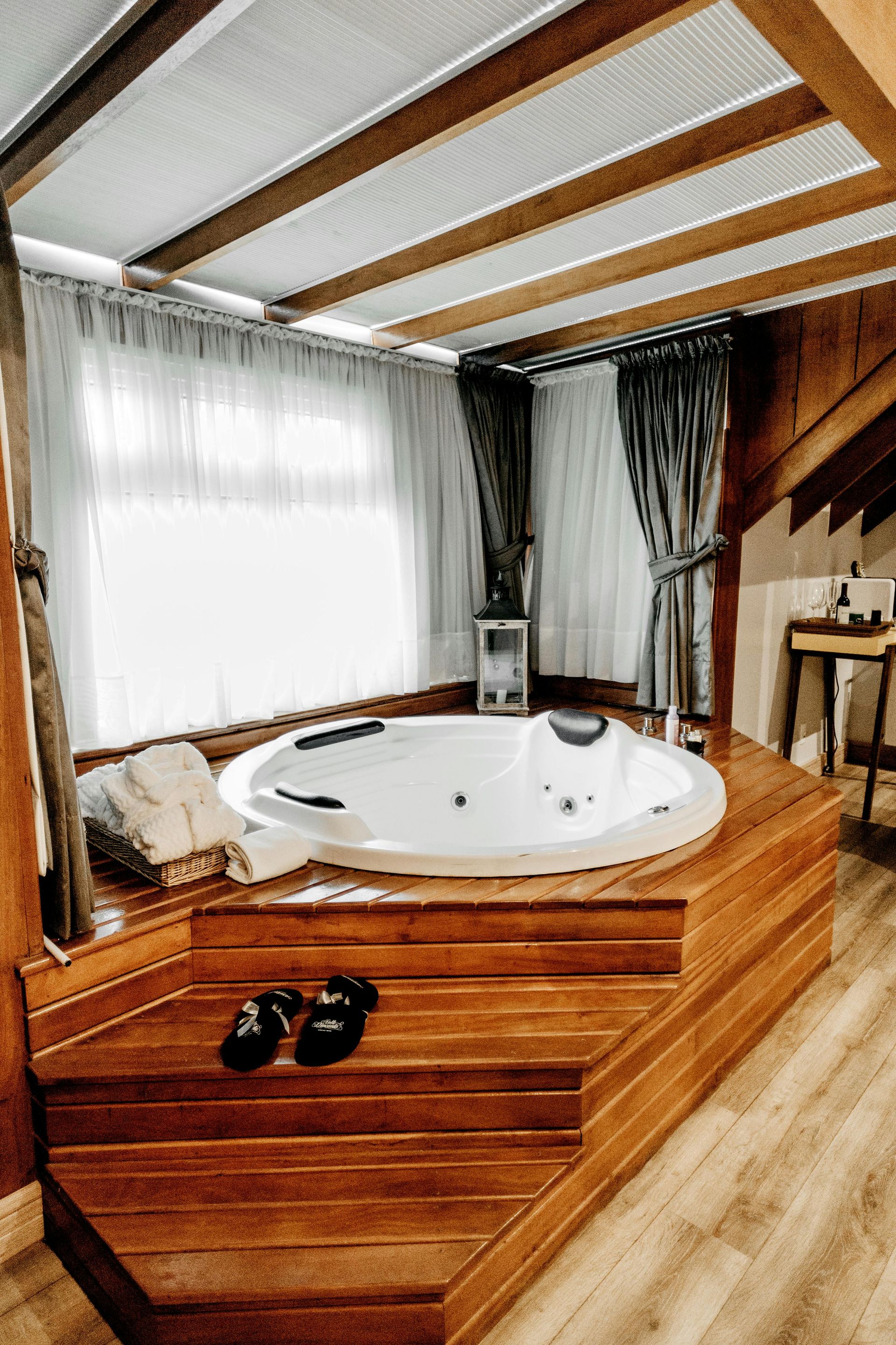 Indoor jacuzzi in a wooden enclosure with steps, next to a window with curtains.