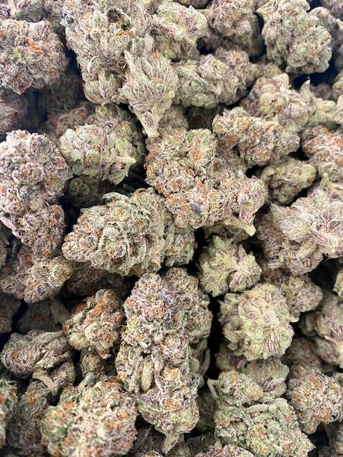 Close-up of trimmed cannabis buds, showcasing dense, resin-coated nugs with purple hues, ready for packaging and sale
