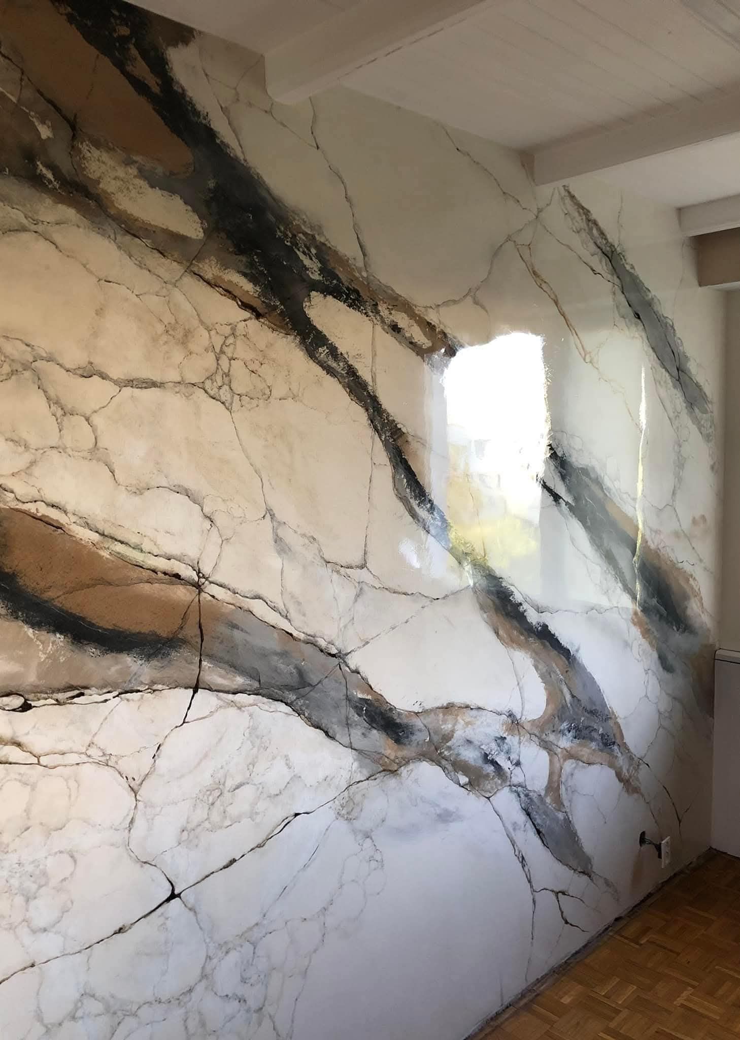 Murale astratto moderno con venature nere e dorate su una parete beige vicino a una finestra