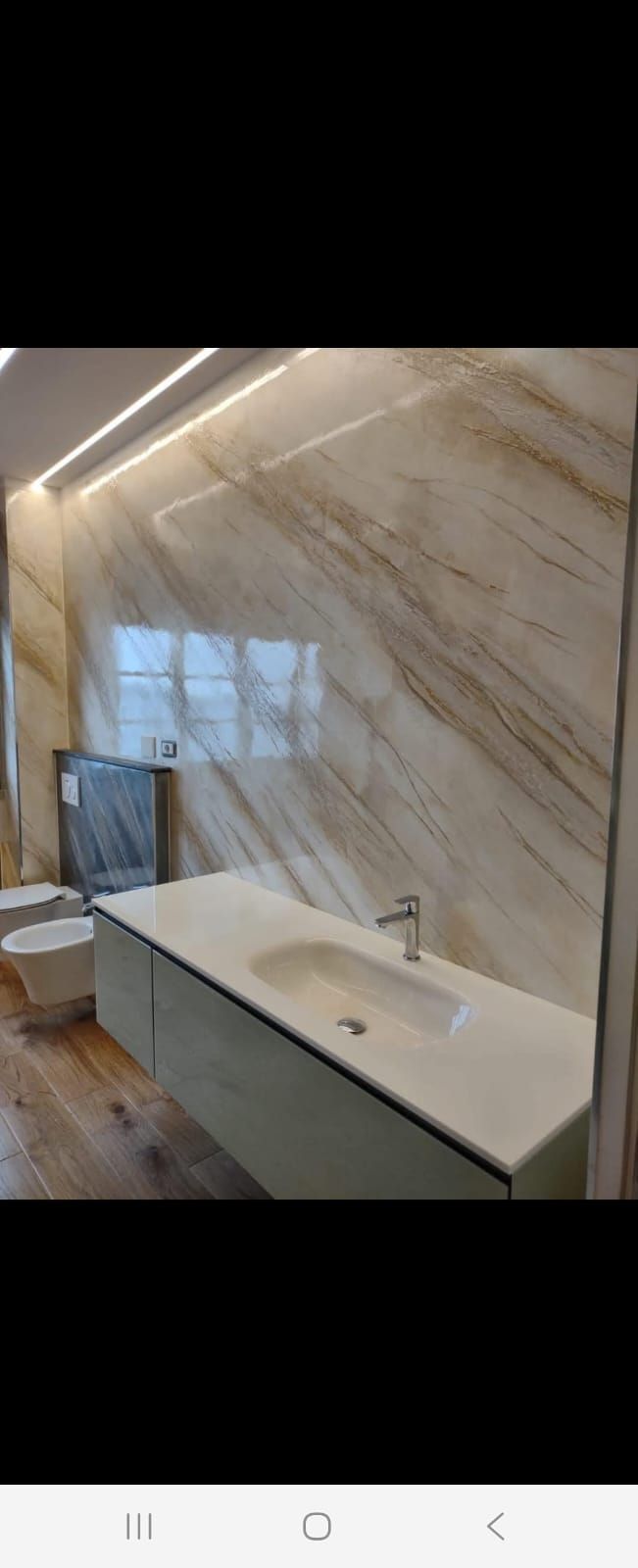 Bagno moderno con rivestimento in marmo, mobile lavabo sospeso, specchio e illuminazione a LED a luce calda.