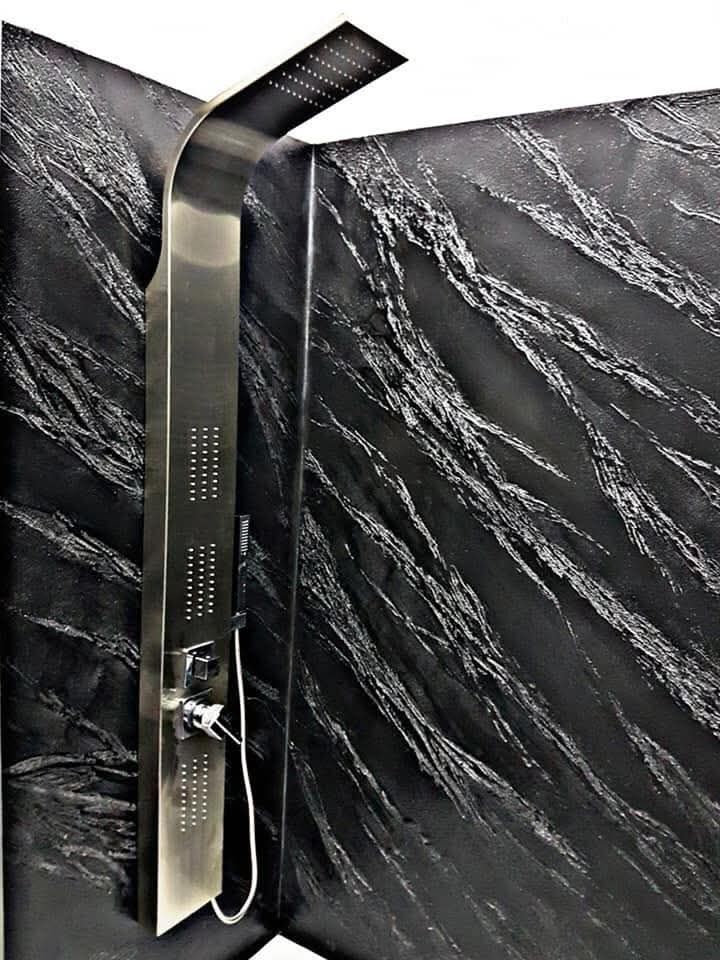 Pannello doccia nero a parete con beccuccio superiore curvo e doccetta a mano su una parete in marmo.