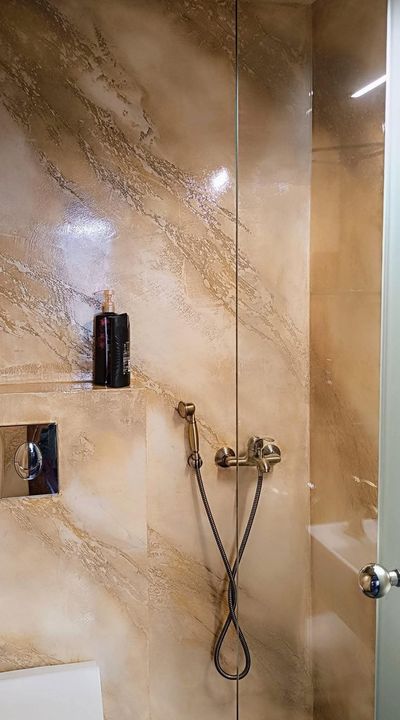 Doccia con piastrelle in marmo beige, doccetta a mano cromata e dispenser di sapone a parete.
